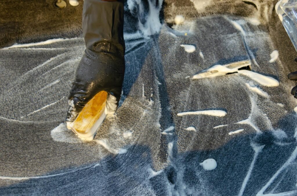 A detailed view of cleaning in progress, focusing on a gloved hand using a brush with detergent on a surface.